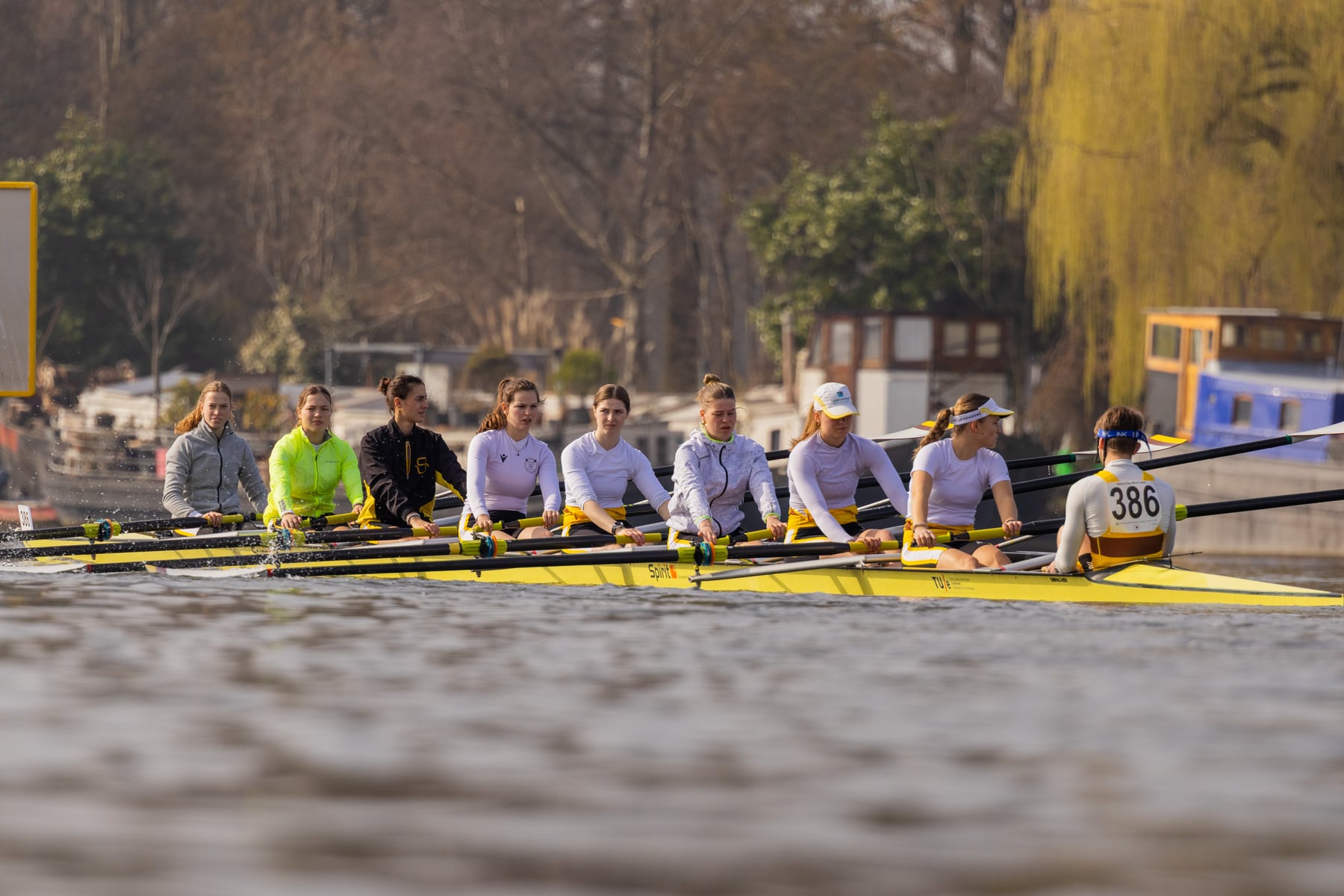 A rowing crew driving together past the riverbank in bright spring light.