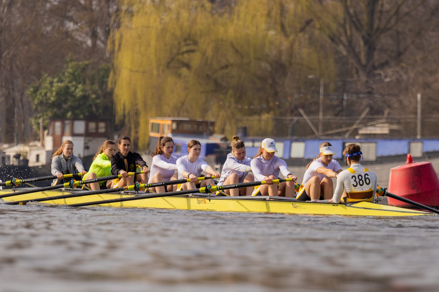 Crew members rowing in sync with yellow blades over rippled water.