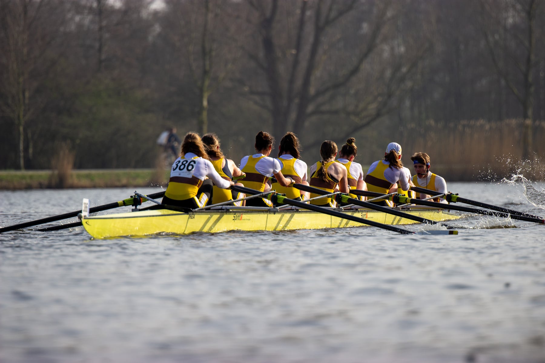 Two crews racing close together on open water under spring trees.