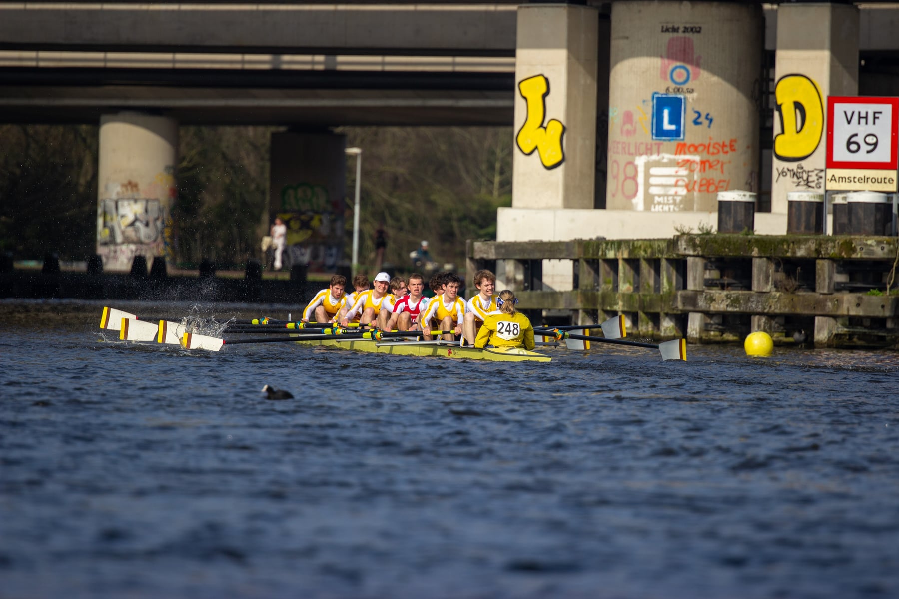 A crew passing under a bridge with yellow blades visible in rhythm.