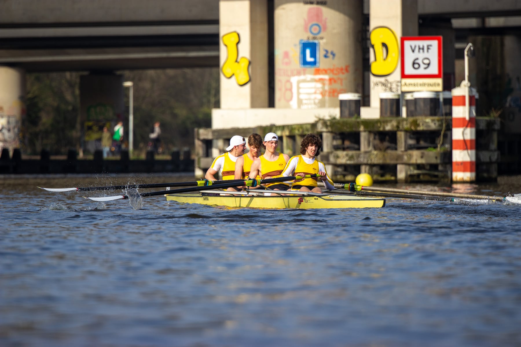 A crew rowing out from the bridge with bright blades and strong reflections.