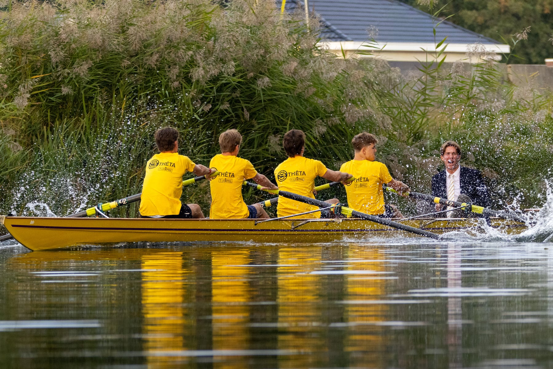A rowing crew moving along a green riverbank during Herfstregatta.
