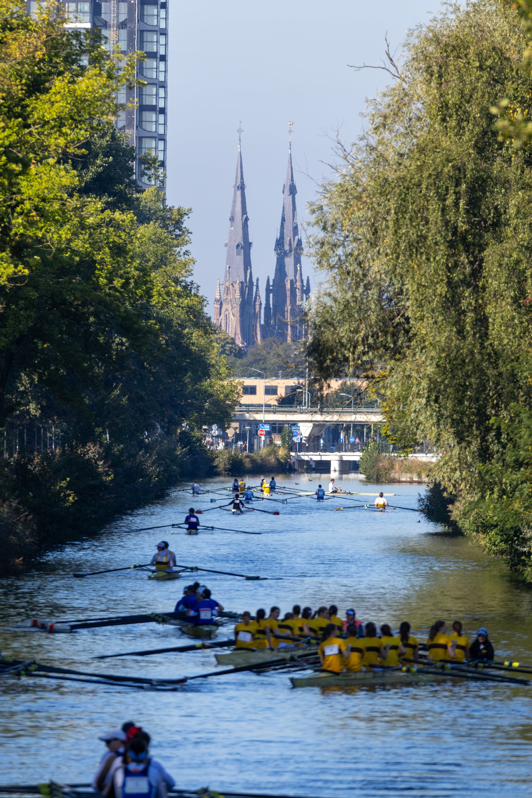 A long canal view with small rowing shells moving through a leafy course.
