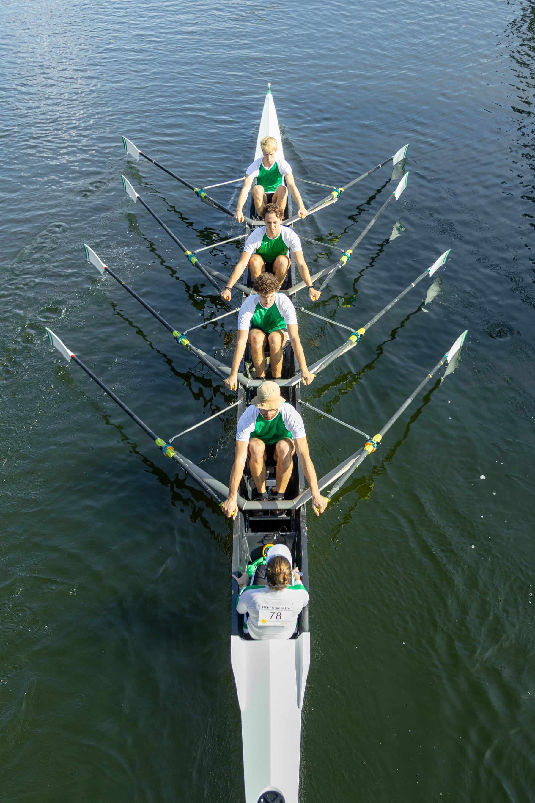 An overhead view of a green crew aligned in a narrow rowing shell.