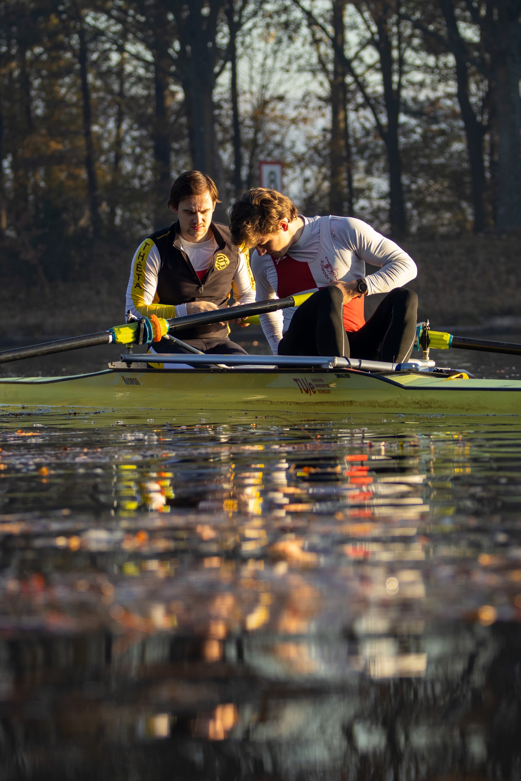 Rowers preparing beside the water with oars cutting through golden reflections.