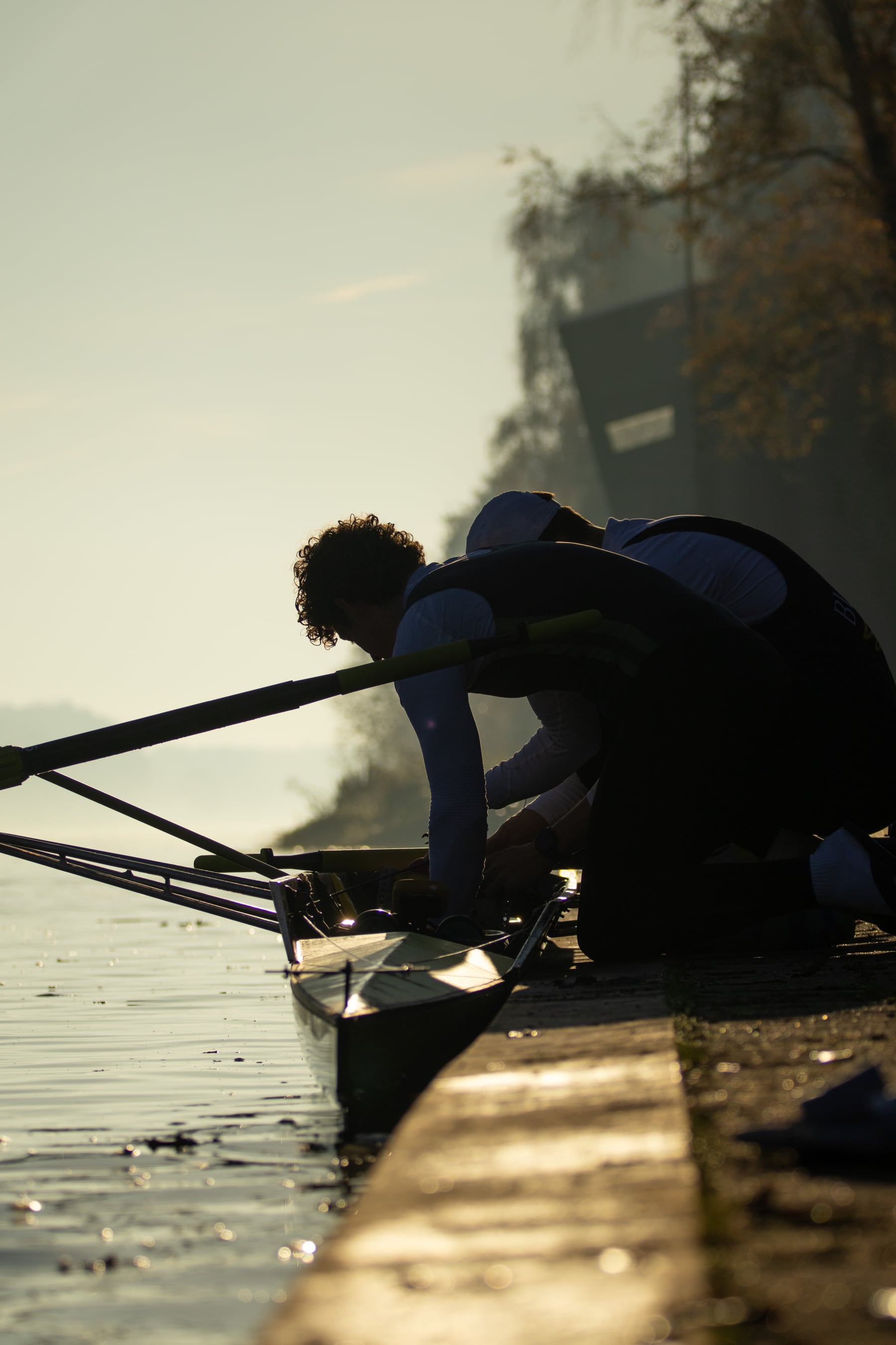 A rower leaning over the shell in dark silhouette before training.
