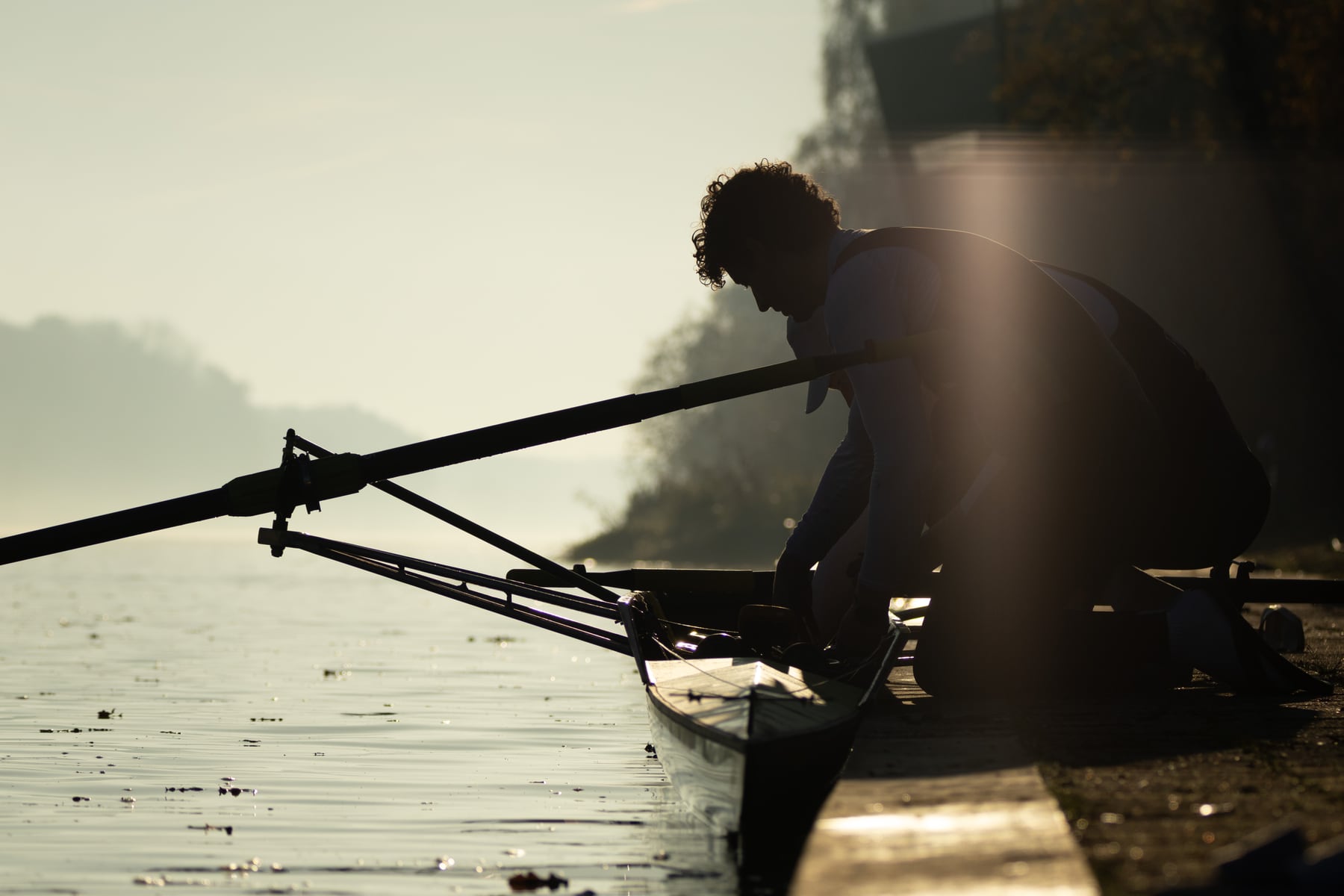 A close low-angle silhouette of a rower and oar above the water.