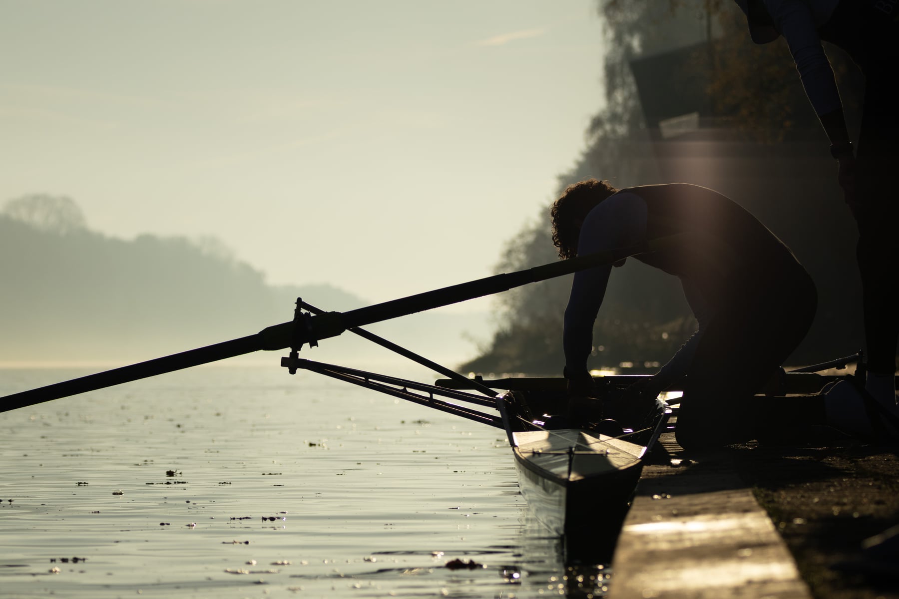 A crew member focused in the shell with blurred oars crossing the foreground.