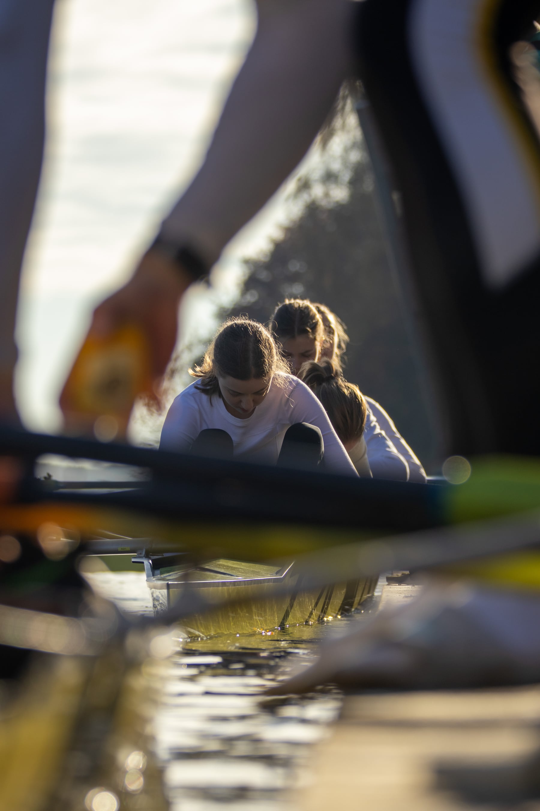 A low-angle view of athletes rowing past warm reflections and shoreline.