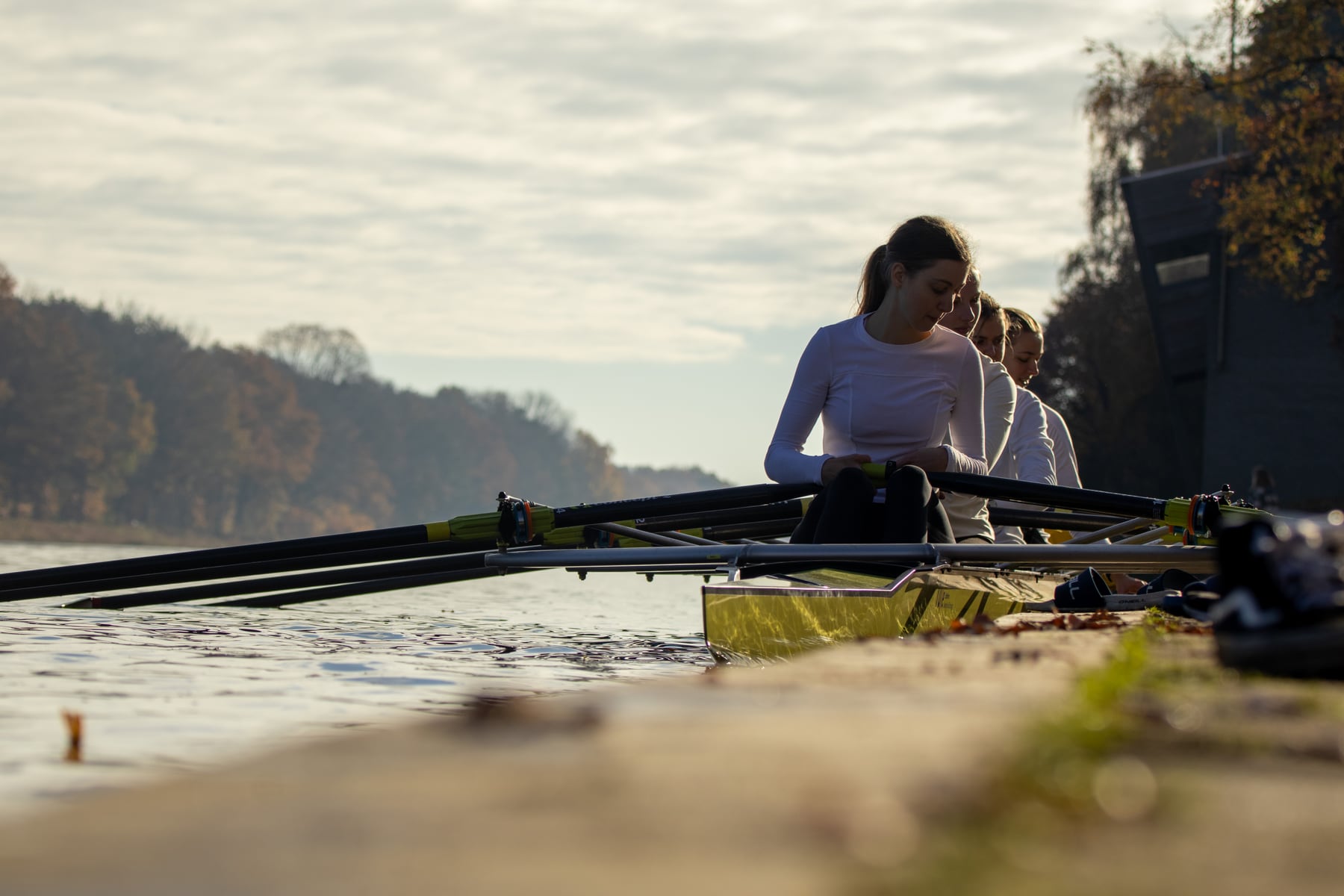 Two rowers moving beside the bank with a long oar crossing the frame.