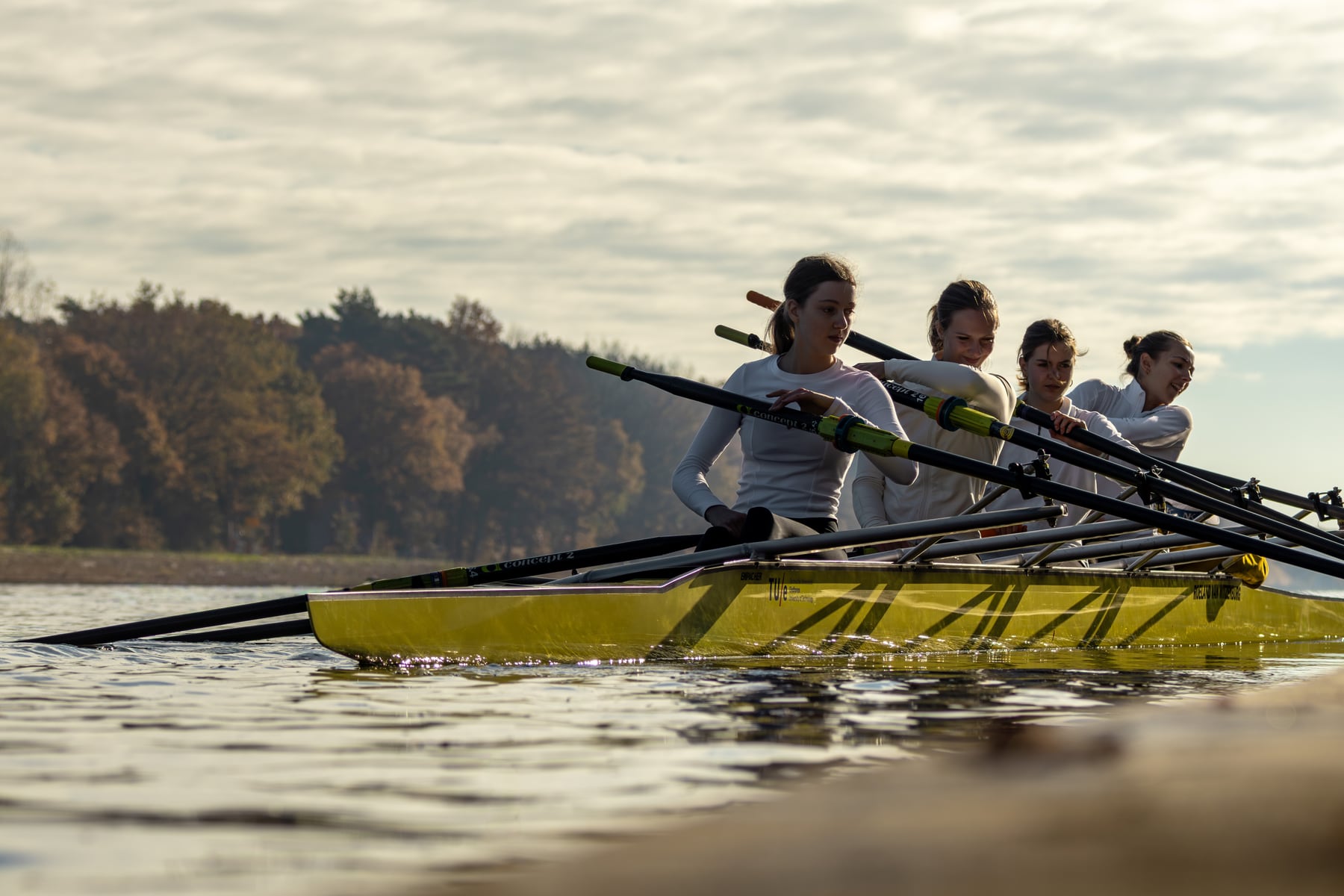 A yellow shell with a crew rowing in profile across calm water.